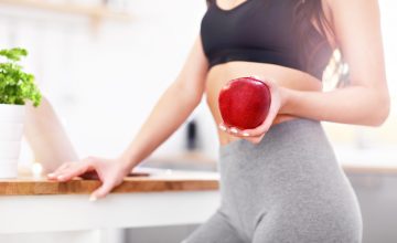 Imagen que muestra la mujer joven en forma con manzana en la cocina moderna